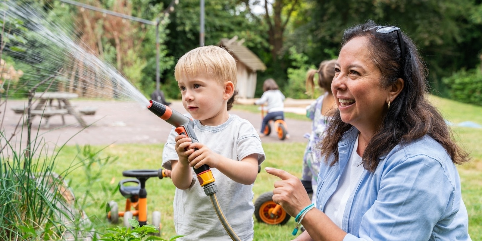 Child waters garden with childcare teacher